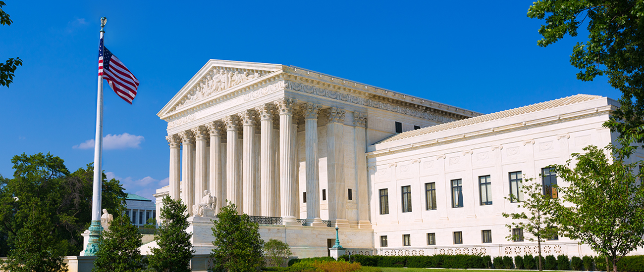 The front facade of the United States Supreme Court building with an American flag in the foreground.